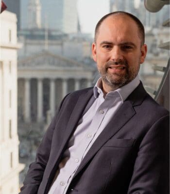 Robert King, CEO von Acuity Knowledge Partners - Der Mann in Anzug und Hemd sitzt vor einem Fenster mit Blick auf ein historisches Gebäude im Hintergrund. Die Szenerie vermittelt einen professionellen Kontext, möglicherweise in einem Büro. Die Beleuchtung ist natürlich und betont die Gesichtszüge von Robert King, CEO von Acuity Knowledge Partners.