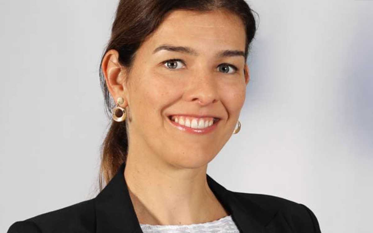 Eine Person mit langen, braunen Haaren und einem freundlichen Lächeln ist abgebildet. Sie trägt einen schwarzen Blazer und große Ohrringe. Der Hintergrund ist neutral. Diese Darstellung könnte im Kontext des Innovationsmanagements relevant sein.