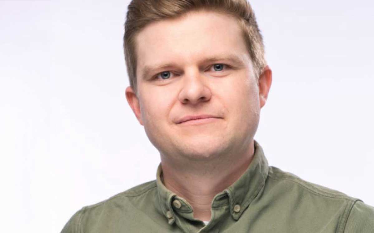 Ein Mann mit kurzen, blonden Haaren und einem grünen Hemd blickt direkt in die Kamera. Der Hintergrund ist neutral und hell. Diese Darstellung könnte im Kontext des Innovationsmanagements stehen, um die Bedeutung von Agilität und neuen Ideen zu betonen.