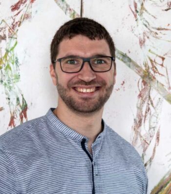 Dr. Alexander Lück, Verantwortlicher für das LLM Benchmarking und PO bei Insiders Technologies, lächelt vor einer künstlerischen Wandgestaltung. Der Fokus liegt auf seiner professionellen Ausstrahlung und der Bedeutung von LLMs in der Versicherungswirtschaft.