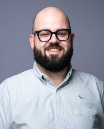 Maximilian Treml lächelt in die Kamera. Er trägt ein hellblaues Hemd und hat einen Bart. Die Abbildung könnte im Kontext der Diskussion um Self-Service-Angebote im Bankwesen stehen, da viele Kunden diese bevorzugen, jedoch oft auf telefonischen Kontakt zurückgreifen