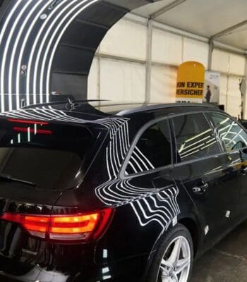 Ein schwarzes Fahrzeug steht unter einer Lichtinstallation, die zur Schadensbewertung dient. Die VHV Allgemeine Versicherung nutzt diese Technologie zur präzisen Begutachtung von Hagelschäden, um den Prozess effizienter zu gestalten.